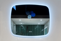 Badkamerspiegel met ingebouwde LED-verlichting die een moderne badkamer weerspiegelt met donkergroene visgraattegels.