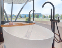 Vrijstaand ligbad met zwarte kraan en houten badplank met accessoires, geplaatst in een moderne badkamer met panoramararaam.