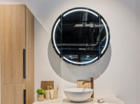 Moderne badkamer met ronde verlichte spiegel, witte waskom en goudkleurige kraan op een licht werkblad, gecombineerd met houten accenten.