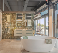 Luxe badkamer met vrijstaand wit bad, marmerlook wanden, dubbele wastafel met spiegels en inloopdouche met zwarte accenten.